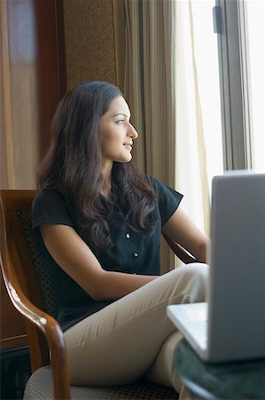 Businesswoman sitting on a chair in front of a laptop in a hotel Stock Photo - Premium Royalty-Free, Code: 630-01708445