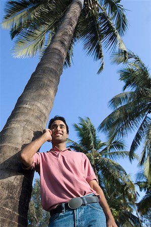 polo shirt - Low angle view of a young man leaning against a tree and talking on a mobile phone Foto de stock - Sin royalties Premium, Código: 630-01708657
