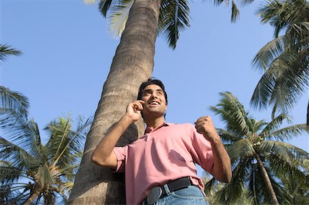 palm fronds clothing - Low angle view of a young man leaning against a tree and talking on a mobile phone Stock Photo - Premium Royalty-Free, Code: 630-01708659