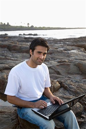 Portrait of a young man holding a laptop on his lap and smiling, Madh Island, Mumbai, Maharashtra, India Stock Photo - Premium Royalty-Free, Code: 630-01708665