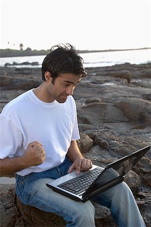 Young man working on a laptop on a coast, Madh Island, Mumbai, Maharashtra, India Foto de stock - Sin royalties Premium, Código: 630-01708666