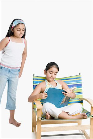 full photo in girls in studio - Girl holding a magazine with her sister standing behind her Stock Photo - Premium Royalty-Free, Code: 630-01709119