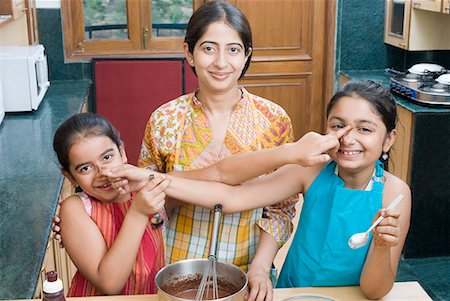 simsearch:630-01709141,k - Portrait of a mid adult woman baking chocolate sauce with her daughters touching each other's nose Foto de stock - Royalty Free Premium, Número: 630-01709139