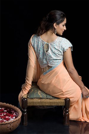 Rear view of a mid adult woman in lehenga choli and sitting on a stool with a bowl of petals Stock Photo - Premium Royalty-Free, Code: 630-01710037