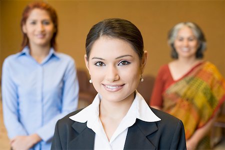 simsearch:628-02954142,k - Portrait of a businesswoman smiling with two businesswomen standing behind her Fotografie stock - Premium Royalty-Free, Codice: 630-01874010