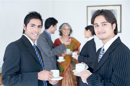Portrait of two businessmen holding cups of tea with their colleagues standing behind them Stock Photo - Premium Royalty-Free, Code: 630-01874030