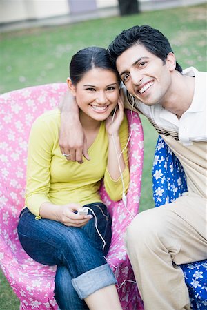 Portrait of a young couple sitting on chairs and listening to an MP3 player Stock Photo - Premium Royalty-Free, Code: 630-01874253