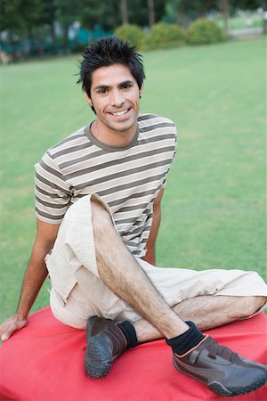 Portrait of a young man sitting on a table in a lawn and smiling Stock Photo - Premium Royalty-Free, Code: 630-01874265