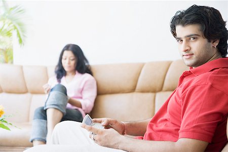 Side profile of a young man holding a mobile phone with a young woman sitting beside him Stock Photo - Premium Royalty-Free, Code: 630-01874568