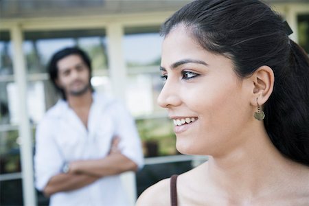 Close-up of a young woman smiling with a young man standing in the background Stock Photo - Premium Royalty-Free, Code: 630-01874920