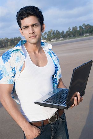Portrait of a young man standing on the beach and holding a laptop Stock Photo - Premium Royalty-Free, Code: 630-01875124