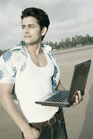 Close-up of a young man standing on the beach and holding a laptop Stock Photo - Premium Royalty-Free, Code: 630-01875123