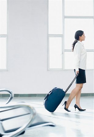 enfoque en el fondo - Side profile of a businesswoman pulling her luggage at an airport Foto de stock - Sin royalties Premium, Código: 630-01875857