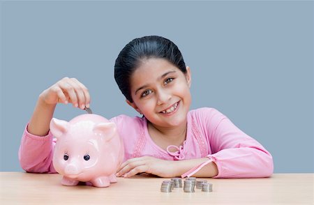 Portrait of a girl putting a coin into a piggy bank and smiling Stock Photo - Premium Royalty-Free, Code: 630-01876437