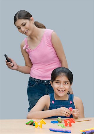 Portrait of a girl smiling and her mother holding a mobile phone behind her Stock Photo - Premium Royalty-Free, Code: 630-01876446