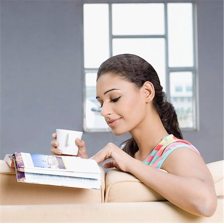 Young woman sitting on a couch and reading a magazine Stock Photo - Premium Royalty-Free, Code: 630-01876633