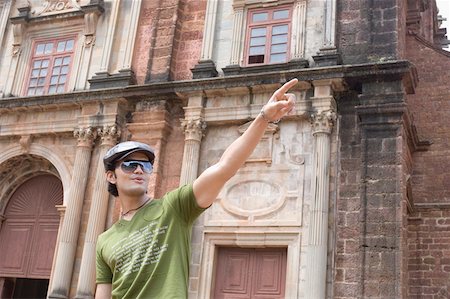 Young man standing in front of a building and pointing, Goa, India Stock Photo - Premium Royalty-Free, Code: 630-01876654