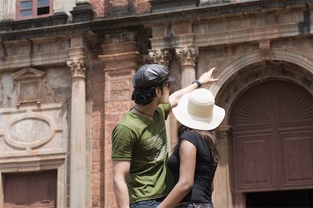 Side profile of a young man standing with a young woman and pointing towards a building, Goa, India Stock Photo - Premium Royalty-Free, Code: 630-01876659