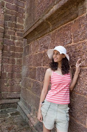 Young woman standing by a stone wall and smiling, Goa, India Stock Photo - Premium Royalty-Free, Code: 630-01876679