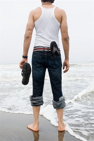 simsearch:630-01877039,k - Rear view of a young man standing on the beach with holding a flip- flop Fotografie stock - Premium Royalty-Free, Codice: 630-01876880