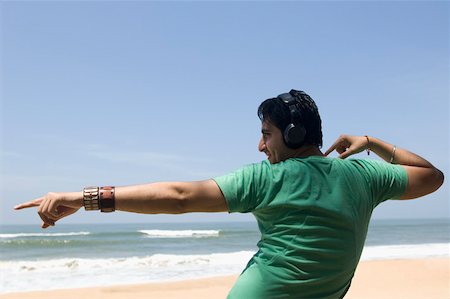 simsearch:630-01877039,k - Rear view of a young man wearing headphones and dancing on the beach Fotografie stock - Premium Royalty-Free, Codice: 630-01877029