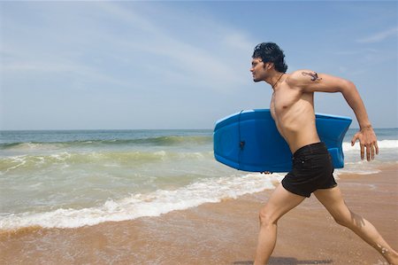 Young man carrying a surfboard and running on the beach Stock Photo - Premium Royalty-Free, Code: 630-01877080