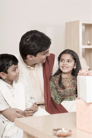 family celebrating diwali - Young man sitting with his son and daughter behind lamps lit on a wooden table Stock Photo - Premium Royalty-Free, Code: 630-01877211