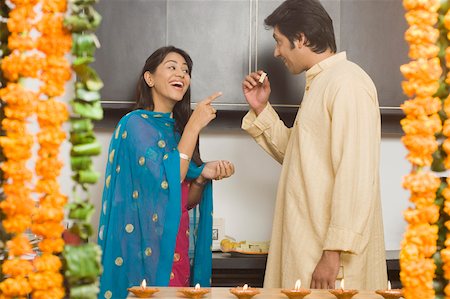 Side profile of a mid adult man eating a piece of burfi and a young woman pointing towards him Stock Photo - Premium Royalty-Free, Code: 630-01877335