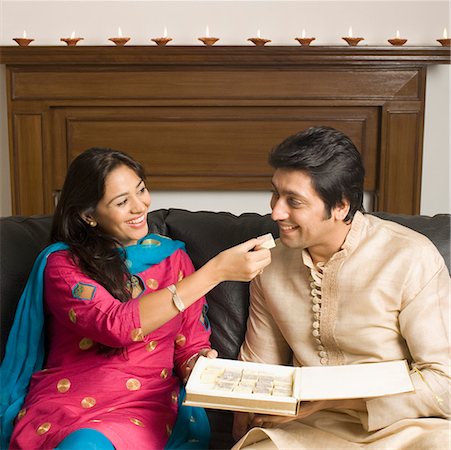 diwali sweets with people - Close-up of a young woman feeding a piece of burfi to a mid adult man and smiling Stock Photo - Premium Royalty-Free, Code: 630-01877376