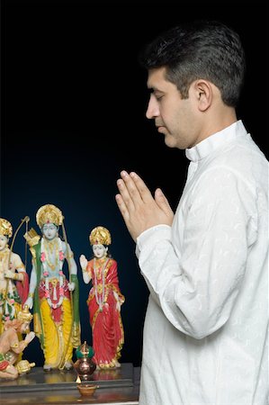Side profile of a mid adult man praying in front of figurines of God Stock Photo - Premium Royalty-Free, Code: 630-01877588
