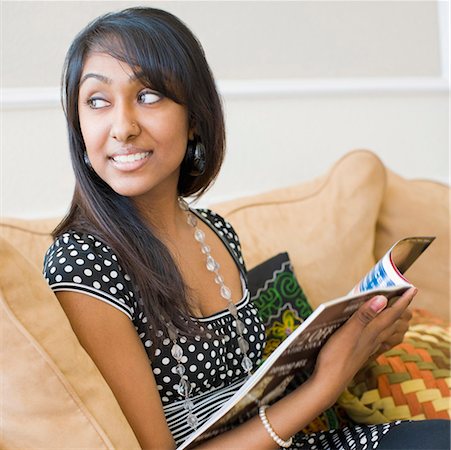 Close-up of a teenage girl sitting on a couch and holding a magazine Stock Photo - Premium Royalty-Free, Code: 630-01877684