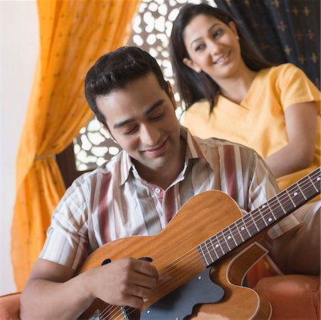 Young man playing a guitar with a young woman sitting behind him Stock Photo - Premium Royalty-Free, Code: 630-01872258