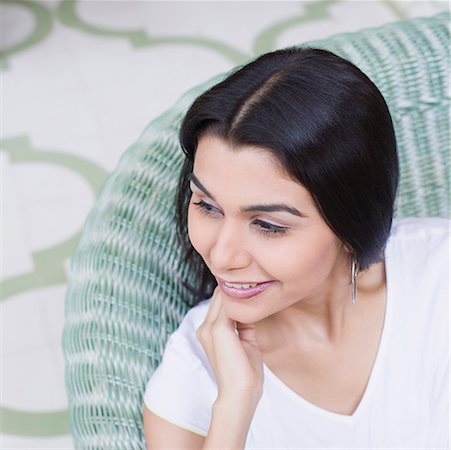 Close-up of a young woman sitting on a couch with her hand on her chin and smiling Stock Photo - Premium Royalty-Free, Code: 630-01872306