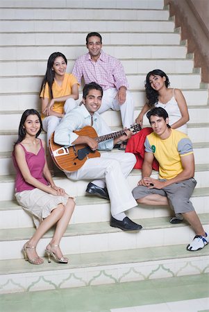 Young man playing a guitar with his friends sitting around him Foto de stock - Sin royalties Premium, Código: 630-01872338