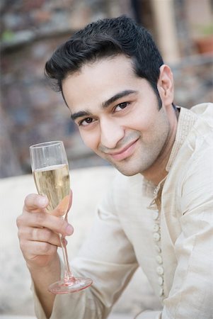 Portrait of a young man holding a champagne flute and smiling Stock Photo - Premium Royalty-Free, Code: 630-01872535