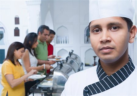 simsearch:630-01872567,k - Portrait of a chef with two mid adult couples having lunch in the background Foto de stock - Sin royalties Premium, Código: 630-01872778