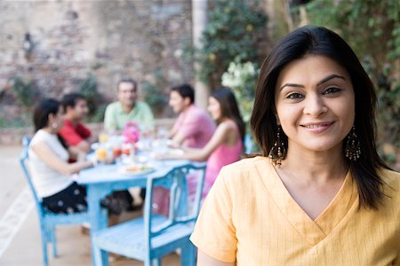 simsearch:630-01872828,k - Portrait of a mid adult woman smiling with her friends sitting at a dining table in the background Foto de stock - Royalty Free Premium, Número: 630-01872824