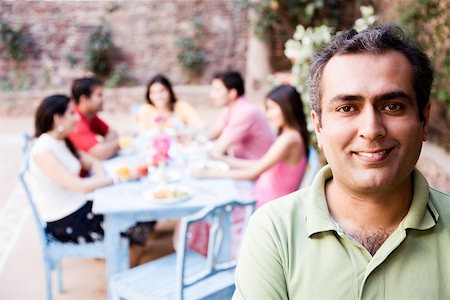 Portrait d'un homme adult mid souriant avec ses amis assis à une table à manger en arrière-plan Photographie de stock - Premium Libres de Droits, Code: 630-01872822