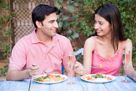 Close-up of a young couple sitting at a dining table and eating food Stock Photo - Premium Royalty-Free, Code: 630-01872840