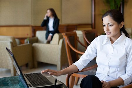 simsearch:630-01873262,k - Businesswoman using a laptop with another businesswoman talking on a mobile phone in the background Stock Photo - Premium Royalty-Free, Code: 630-01873118