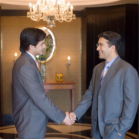 Side profile of two businessmen shaking hands and smiling in a lobby Stock Photo - Premium Royalty-Free, Code: 630-01873197