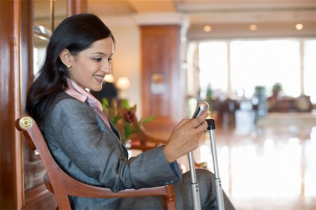 foreground legs - Side profile of a businesswoman text messaging on a mobile phone and smiling Stock Photo - Premium Royalty-Free, Code: 630-01873240