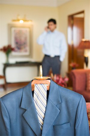 simsearch:630-01708436,k - Business suit hanging on a hanger and a businessman talking on a mobile phone Fotografie stock - Premium Royalty-Free, Codice: 630-01873335