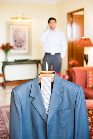 Close-up of a business suit hanging on a hanger with a businessman standing in the background Stock Photo - Premium Royalty-Free, Code: 630-01873336