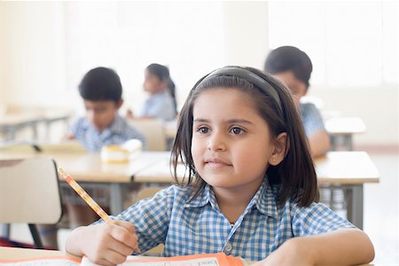 Close-up of a schoolgirl sitting at a desk with other students in the background Stock Photo - Premium Royalty-Free, Code: 630-01873572