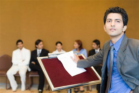 simsearch:630-01873857,k - Portrait of a businessman standing at a lectern with his colleagues in the background Foto de stock - Royalty Free Premium, Número: 630-01873936