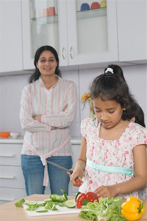 simsearch:630-02219554,k - Close-up of a girl cutting vegetables on a cutting board with her mother standing behind her Foto de stock - Sin royalties Premium, Código: 630-02219743