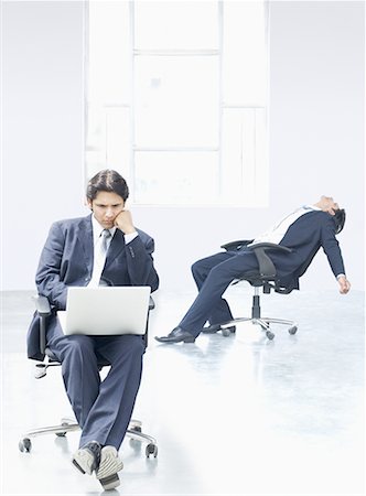 Businessman using a laptop with another businessman reclining on a chair in an office Stock Photo - Premium Royalty-Free, Code: 630-02219979