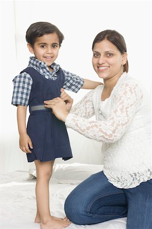 Portrait of a mid adult woman helping her daughter in wearing school uniform and smiling Stock Photo - Premium Royalty-Free, Code: 630-02220187
