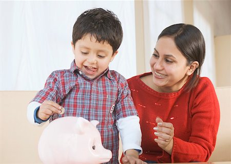 Garçon de mettre une pièce de monnaie dans une tirelire avec sa mère assise à côté de lui Photographie de stock - Premium Libres de Droits, Code: 630-02220217